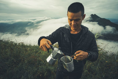 Man pouring black tea in jug while standing on field