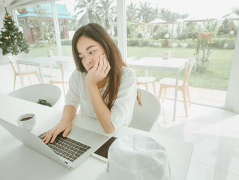 Young woman using laptop while sitting on table