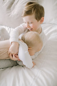 Toddler boy and baby sister playing on bed at home