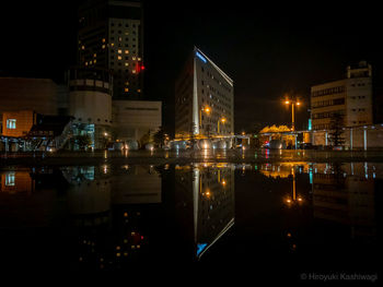 Illuminated buildings by river against sky at night