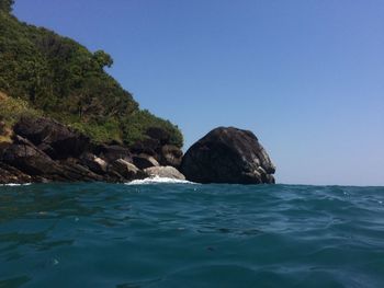 Rock formation in sea against clear blue sky