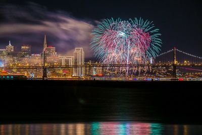 Firework display and illuminated cityscape by san francisco–oakland bay bridge