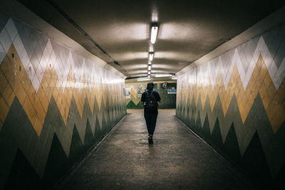Rear view of man walking in illuminated tunnel