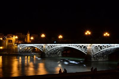 Illuminated bridge over river against sky in city at night