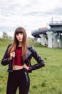 Fashionable young woman standing on field with bridge in background