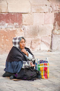 Full length portrait of woman sitting against brick wall