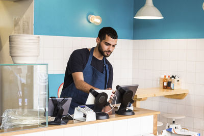 Confident young owner using digital tablet at checkout in restaurant
