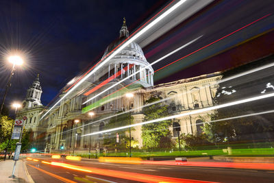 Light trails on illuminated city against sky at night