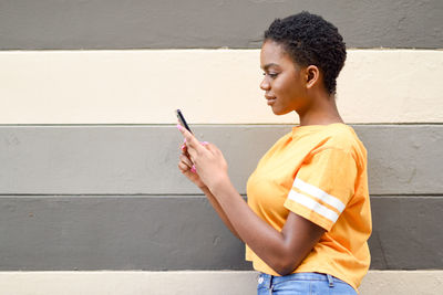 Side view of woman using phone standing against wall