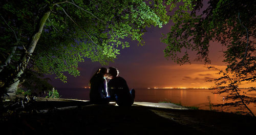 Rear view of couple sitting at beach during sunset