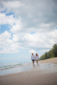 Man and woman walking at beach against sky