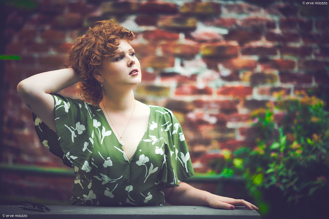 one person, women, adult, young adult, fashion, hairstyle, relaxation, looking, sitting, contemplation, female, portrait, nature, portrait photography, elegance, redhead, brick, clothing, lifestyles, beauty in nature, arts culture and entertainment, photo shoot, copy space, person, curly hair, wall, green, brown hair, brick wall, architecture