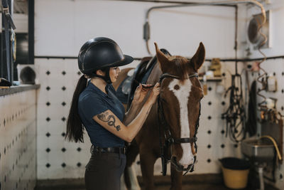 Woman in stable preparing horse for horse riding
