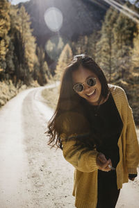 Young woman wearing sunglasses holding cigarette while standing against forest path