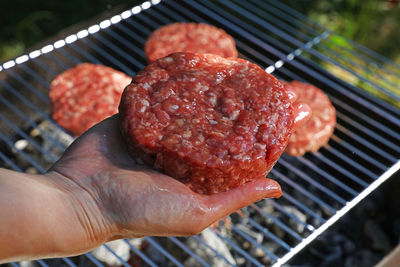 Close-up of cropped hand holding meat on barbecue grill