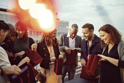 Happy business colleagues checking gift bags while enjoying office party on terrace