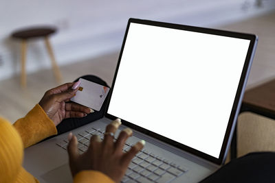 Young woman holding credit card while using laptop doing online shopping at home