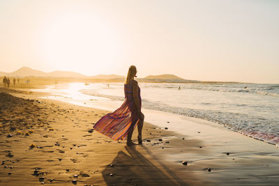 Rear view of woman on beach against sky during sunset