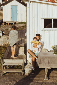 Smiling father embracing baby girl while boy covered in blanket walking by cabin