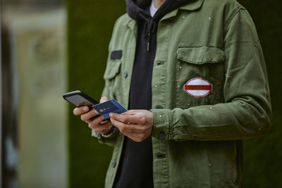 Man in jacket holding mobile phone while doing online shopping through credit card