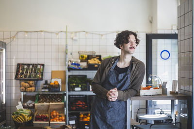 Male owner looking away while leaning on table at store