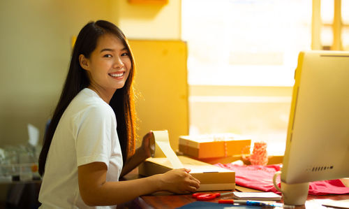 Portrait of smiling young woman using phone while sitting on table