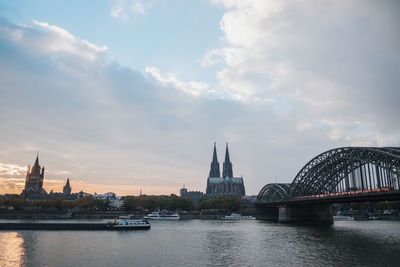 Bridge over river in city against cloudy sky