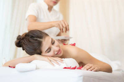 Masseur putting flower petals on young woman in spa