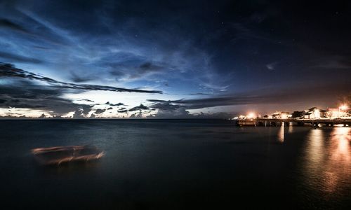 Scenic view of illuminated city against cloudy sky at dusk