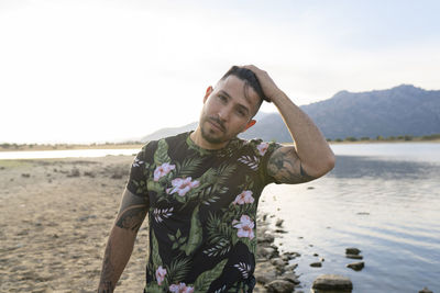 Portrait of young man standing on beach against sky