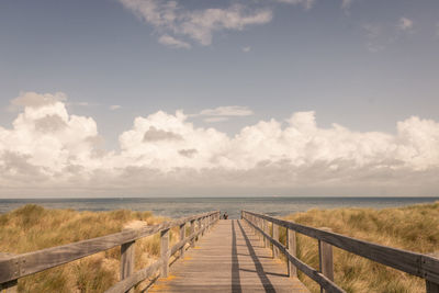 Scenic view of pier, sea and dunes against sky