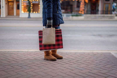 Low section of woman holding shopping bags on sidewalk during christmas holiday season