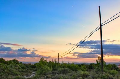 Electricity pylon on land against sky during sunset