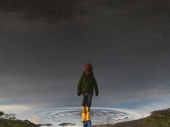 Upside down image of girl standing in water against sky