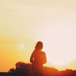 Silhouette of woman standing against sky at sunset