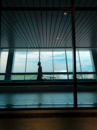 Silhouette man standing at airport seen through glass window