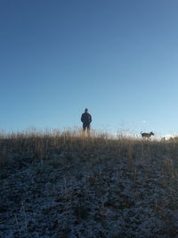 Man with dog standing on field against clear blue sky during winter