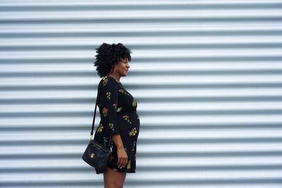 Side view of mid adult woman with shoulder bag standing against wall