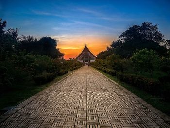 Walkway amidst trees against sky during sunset