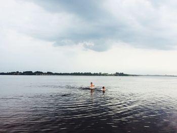 Boys and girls playing in sea against sky