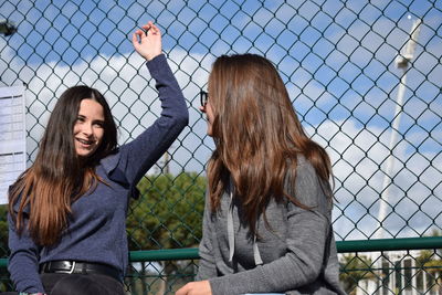 Beautiful young woman standing by chainlink fence