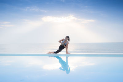 Full length of young woman exercising by infinity pool against sea against sky