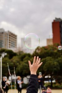 Cropped hand of woman reaching to bubble at park