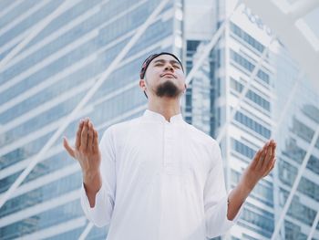 Low angle view of man praying while standing against building