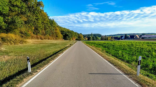 Country road amidst plants and trees against sky
