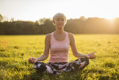 Senior woman in lotus position on rural meadow at sunset