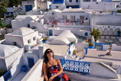 High angle view of mid adult woman wearing sunglasses while sitting on building terrace