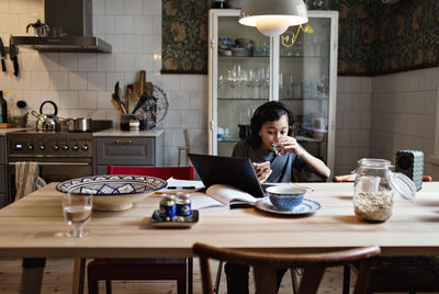 Boy drinking water while using laptop for homework at home