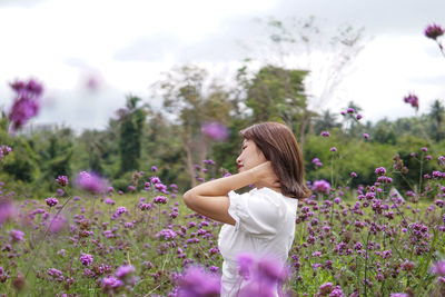 Side view of young woman standing amidst purple flowering plants