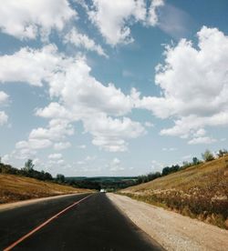 Empty road amidst field against sky